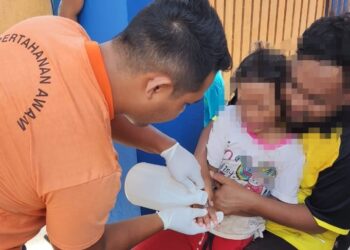ANGGOTA Pertahanan Awam Besut meletakkan cuka di tangan kanak-kanak yang terkena sengatan obor-obor merah ketika bermain bot pisang di Pantai Bukit Keluang di Besut, semalam.