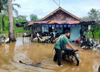 MOHD. Fadhlan Jaafar menolak motosikal pelanggan selepas bengkelnya di Kampung Paya Rumput, Tangga Batu, Melaka dilanda banjir kilat. - UTUSAN/DIYANATUL ATIQAH ZAKARYA