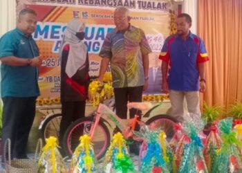 MAHDZIR Khalid (dua kanan) menyampaikan hadiah cabutan bertuah berupa sebuah basikal kepada seorang pelajar SK Tualak sempena Mesyuarat PIBG sekolah itu di Kuala Nerang, Padang Terap di sini.