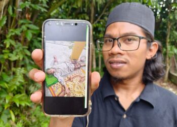 MOHAMAD Nizam Mohamad menunjukkan gambar datuknya yang cedera selepas disondol babi hutan semasa sedang mengutip buah durian di kebun berhampiran rumahnya di Taman Desa Wangi, Kampung Kubang Siput, Pasir Tumboh, Kelantan hari ini. -UTUSAN/ROHANA MOHD.NAWI