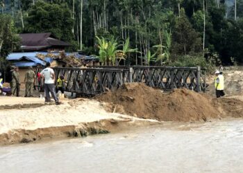 KAKITANGAN Bahagian Jalan dan Cawangan Kerja Mekanikal JKR Kedah sambil dibantu 10 anggota RAJD sedang memasang jambatan sementara di Kampung Iboi, Kupang. -UTUSAN/IQBAL HAMDAN