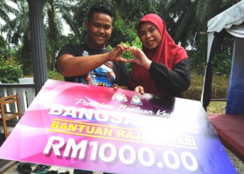 MOHAMAD Aiman Hakim Mohd. Salleh 20, bersama  isteri Nur Asyura Ashri  21, menerima replika cek bernilai RM1000 bagi penerima bantuan kasih Bangsa Johor Raja Sehari sempena Majlis Korban Perdana di Rumah Orang Semerah, Semerah Batu Pahat disini.-UTUSAN/RAJA JAAFAR ALI