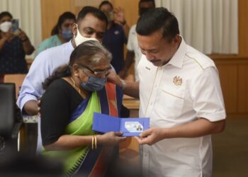 R. ALLIAMAH, 64, yang sebak ditenangkan anaknya, Mohd. Faizal Suresh Abdullah, 45,  ketika menerima MyKad daripada Ruslin Jusoh di Bangunan Persekutuan, Jalan Anson, Georgetown, Pulau Pinang hari ini.