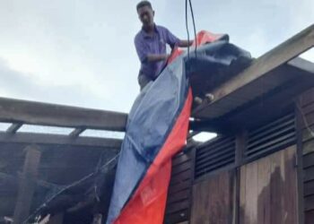 SEORANG penduduk menutup bahagian bumbung rumahnya yang rosak dengan kanvas akibat ribut di Bandar Al-Muktafi Billah Shah, Dungun, hari ini. - UTUSAN/NIK NUR IZZATUL HAZWANI NIK ADNAN