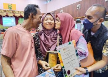 NUR RAIDAH Abdul Majid dicium kedua ibu bapanya ketika meraikan kejayaannya muncul antara pelajar cemerlang STPM 2021 peringkat negeri Melaka. - UTUSAN/MUHAMMAD SHAHIZAM TAZALI