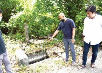 THEENATAYALAN Manoharah menunjukkan longkang yang tersumbat akibat dari akar pokok yang menjalar di dalamnya sambil diperhatikan Mohd. Najwan Halimi dekat Taman Mutiara Bukit Raja di Klang, Selangor. – Utusan/ZULFADHLI ZAKI