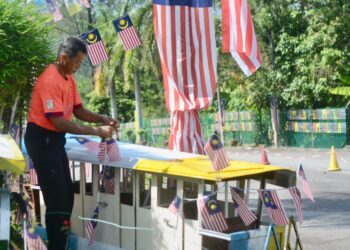 ROSLAN Mohd. Hashim (baju oren) sedang memperkemaskan hiasan bertemakan kemerdekaan yang dihasilkannya menggunakan botol mineral terpakai di Sekolah Kebangsaan (SK) Sungai Batu, Teluk Kumbar.
