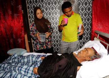 Mohammad Nasrul (kanan) memberi minuman susu melalui tiub kepada bapanya Ramli Ibrahim yang terlantar sakit sambil diperhatikan oleh ibunya Anita Mohd Salleh di rumahnya di Blok D, Taman Perling, Johor  Bahru. – UTUSAN/RAJA JAAFAR ALI