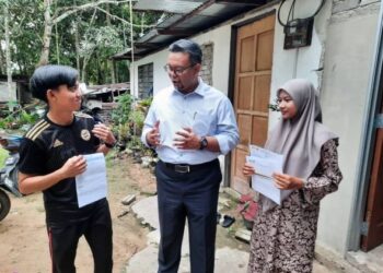 HAIM Hilman Abdullah (tengah) memberi surat tawaran kepada Muhammad Omar Mokhtar Abdul Rahman dan Salmah Aminudin agar meneruskan pengajian ke universiti ketika lawatan 
di Pokok Sena, di sini semalam  – UTUSAN/MOHD RIFAAT ABD HAMID