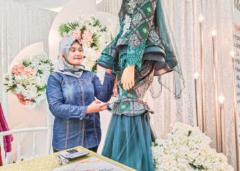 NUR FATEHAH Mazelan melihat persalinan pengantin yang dipamerkan di kiosnya sempena Festival Pengantin AEON 
2022. – UTUSAN/MUHAMMAD SHAHIZAM TAZALI