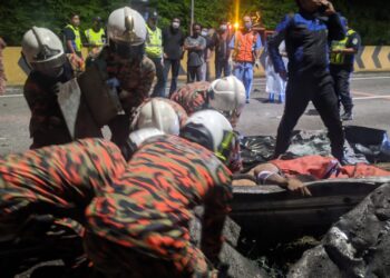 ANGGOTA bomba mengangkat mayat pemandu lori yang tersepit pada pembahagi jalan dalam kejadian di Kilometer 257, Lebuh Raya Utara-Selatan arah utara dekat Kuala Kangsar hari ini. - UTUSAN/JBPM PERAK