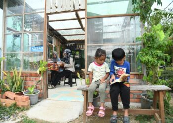 DUA kanak-kanak sedang asyik membaca di perpustakaan mini di dalam kampung hasil inisiatif seorang anak muda di Balbuk Haus, Kampung Balik Bukit, Chuping, Padang Besar, Perlis, semalam.- UTUSAN/IZLIZAN OTHMAN