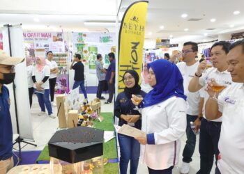 NORLIZA ABDUL RAHIM mendengar penerangan produk daripada salah seorang peniaga yang menyertai Karnival Uda USHAniaga Keluarga Malaysia di Angsana Johor Bahru Mall.