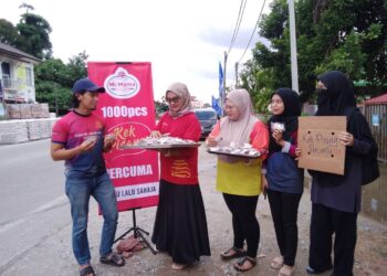 AIMAN Ahmad Farid (kiri) menunjukkan sebiji kek pisang untuk diagihkan kepada pengguna jalan raya di Kampung Pintu Geng, Kota Bharu, Kelantan.-UTUSAN/ROHANA MOHD.NAWI.