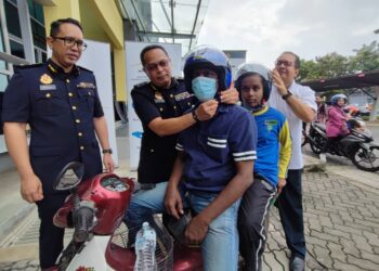 SHAHRUL AZHAR Md. Dali dan Faisal Shahbudin memakaikan topi keledar kepada penunggang dan pembonceng motosikal dalam program CSR JKSB dengan kerjasama JPJ di Batu Kawan, Pulau Pinang hari ini.
