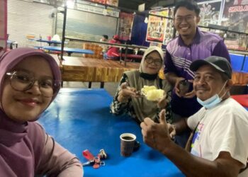 NORSYAZWAN (berdiri) melayan pelanggan yang menikmati ubi rebus yang dijual di Medan Selera Muafakat Kota Tinggi.