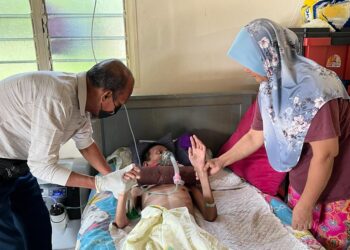 NORIZAN Mahasan (kanan) dan Ismail Dris menguruskan anaknya yang terlantar sakit di Kampung Lepan Jaya, Gua Musang, Kelantan.-UTUSAN/AIMUNI TUAN LAH