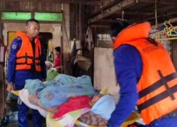 ANGGOTA APM membantu memindahkan  seorang warga emas yang menghidap sakit tua selepas kediamannya dinaiki air di Kampung Bakat, Machang, Kelantan. - IHSAN APM