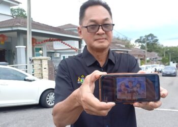 MICHAEL Thai menunjukkan foto empat sekeluarga yang maut dalam tragedi di tapak perkhemahan Father’s Organic Farm di Batang Kali, Selangor. - UTUSAN/AMRAN MULUP