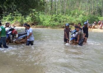 PENDUDUK Orang Asli Pos Balar saling bekerjasama mengusung motosikal ketika melalui Sungai Inching untuk ke bandar Gua Musang, Kelantan. – MINGGUAN/IHSAN PENDUDUK ORANG ASLI.