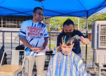 MOHD. RAFIQ Naizamohideen (kiri) melihat seorang pelajar sekolah sedang menggunting rambut pada program gunting rambut percuma untuk pelajar sekolah di Tanjung Minyak, Melaka. - UTUSAN/MUHAMMAD SHAHIZAM TAZALI