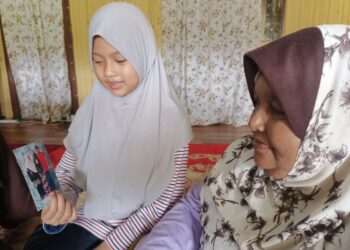SUFIA Az-Zahara (kiri) menunjukkan gambar ibu dan bapa angkatnya kepada Esah Jenal di Kampung Belukar Tebu, Kuala Krai, Kelantan.-UTUSAN