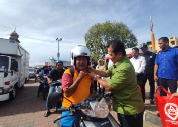 AZMAN Nasrudin memakaikan topi keledar baharu kepada penunggang motosikal pada Majlis Pelancaran Kempen Keselamatan Jalan Raya dan Op Bersepadu Sempena Tahun Baharu Cina Peringkat Kedah di Dataran Zero, Sungai Petani.