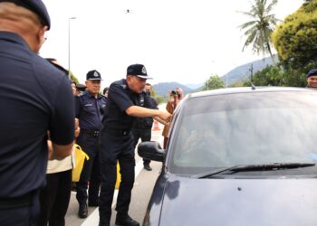 MUHAMMAD Zaki Harun (kiri) menyantuni pemandu semasa turun padang memantau sekatan jalan raya sempena Op Tahun Baru Cina di Bukit Yong, Pasir Putih, Kelantan.UTUSAN/KAMARUL BISMI KAMARUZAMAN