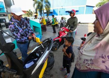 AZLI Mohd. Nor (kiri) membantu mengisi minyak petrol kepada pengguna motosikal di sebuah stesen minyak di Kubang Kerian, Kota Bharu, Kelantan hari ini-UTUSAN/ROHANA MOHD.NAWI