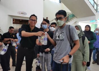 MOHD. Iqmal Muslim (kiri) mengagihkan bubur lambuk kepada penumpang yang tiba di Lapangan Terbang Sultan Ismail Petra, Pengkalan Chepa, Kelantan hari ini-UTUSAN/ROSALWANI CHE SOH