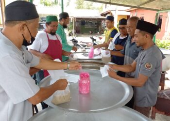 PENDUDUK bergotong-royong membungkus bubur lambuk untuk diagih-agihkan kepada orang ramai secara pandu lalu di Kampung Bukit Piatu, Bukit Baru, Melaka. - UTUSAN/AMRAN MULUP