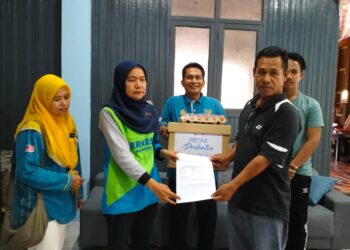 NORA Yaacob (dua kiri) menyerahkan faedah pengurusan jenazah kepada Kamarolzaman Che Ahmad ketika kunjungan PERKESO di rumahnya di Kampung Perupok Chetok Pasir Mas Kelantan.-UTUSAN/ROHANA ISMAIL