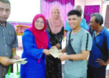 Tuminah Kadi menyampaikan wang ihsan berjumlah RM400 kepada salah seorang nelayan di pejabat Japerun Pantai Kundor, Melaka. 
– UTUSAN/AMRAN MULUP