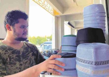 MOHAMED Iman Hakim menyusun kopiah yang dijual di kedainya di Kompleks Bazar El-Medinah, Kota Kinabalu.