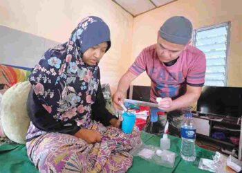 ROHAIZAD Che Soh (kanan) memberi isterinya ubat di rumah mereka di Kampung Kala, Gua Musang, Kelantan. – UTUSAN/AIMUNI TUAN LAH