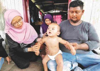 WAN Zalilah Shafie (kiri) melihat keadaan kulit Muhammad Khair Haziq semasa melawat keluarga kanak-kanak berkenaan di Kampung Tanjong Kuala, Tumpat, Kelantan semalam. – UTUSAN/YATIMIN ABDULLAH