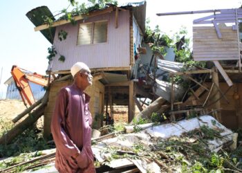 MOHAMED Jali melihat keadaan rumahnya yang dihempap pokok kekabu semasa kejadian ribut di Kampung Pintu Geng, Kota Bharu, Kelantan kelmarin.-UTUSAN/KAMARUL BISMI KAMARUZAMAN
