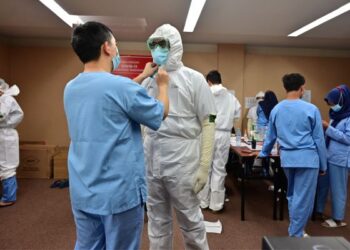 SEORANG doktor membantu rakan sejawatnya mengenakan pakaian perlindungan diri (PPE) bagi menguruskan pesakit Covid-19 di Banten, Indonesia. - AFP