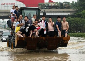 SEJUMLAH penduduk menaiki jentera berat ketika dipindahkan selepas banjir berlaku di bandar Zhengzhou, wilayah Henan, China. - AFP
