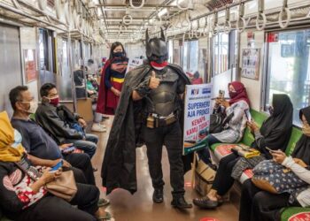 SEORANG lelaki berpakaian kostum Batman membawa sepanduk untuk mengingatkan penumpang tren mengenai langkah pencegahan Covid-19 di Yogyakarta, Indonesia. - AFP