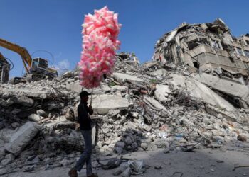 SEORANG penjual gula-gula kapas melintasi bangunan yang musnah dalam konflik Israel-Hamas pada Mei lalu di kawasan kejiranan al-Rimal, Gaza. - AFP