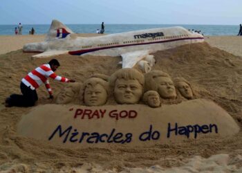 SEORANG artis menyiapkan binaan pasir yang mendoakan kesejahteraan pesawat MH370 di tepi pantai di Puri, India. - AFP