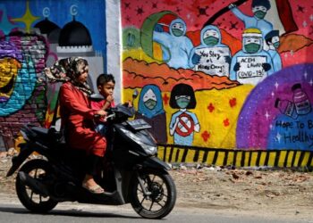 SEORANG wanita dan kanak-kanak menunggang motosikal melintasi mural kesedaran Covid-19 di Banda Aceh, Indonesia. - AFP
