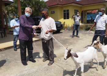 KAMARUDIN Md. Nor (kiri) menyerahkan kambing kepada penerima di Kampung Alor Hijau, Pasir Puteh hari ini.- UTUSAN/TOREK SULONG