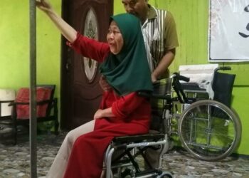 SAFFIE Mamat membantu isterinya, Siti Zaharah Husain duduk di atas kerusi roda di rumah mereka di Kampung Bukit Gemuruh, Hulu Terengganu. - UTUSAN/NOOR HAYATI MAMAT