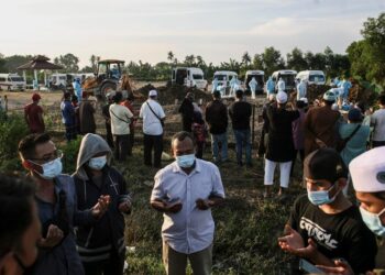 SEKUMPULAN waris mengaminkan bacaan doa terhadap jenazah ahli keluarga mereka ketika dikebumikan di Tanah Perkuburan Selat Klang, Klang, Selangor yang meninggal dunia akibat jangkitan Covid-19. - UTUSAN / ZULFADHLI ZAKI