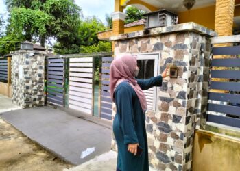 SEORANG wartawan sedang menunggu di luar rumah keluarga Azi di Kampung Semat Jal, Tumpat, Kelantan hari ini. - UTUSAN/ ROHANA ISMAIL