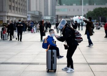 SEORANG wanita membetulkan pelitup muka anaknya ketika tiba di Stesen Kereta Api Hankou di Wuhan, China pada 8 April 2020. - AFP