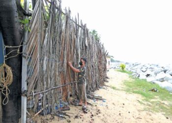 SEORANG penduduk membina penghadang menggunakan pelepah kelapa, di Kampung Pulau Kundur, Kota Bharu, baru-baru ini. - UTUSAN/ROHANA MOHD. NAWI