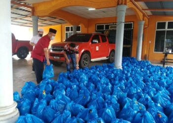 MOHD. Helmi Fakhzan Abd. Wahab (kanan) mengambil bungkusan bakul makanan untuk diagihkan kepada setiap peneroka dan pekerja di Felda Neram 2, Kemaman, Terengganu, hari ini. - FOTO/NIK NUR IZZATUL HAZWANI NIK ADNAN
